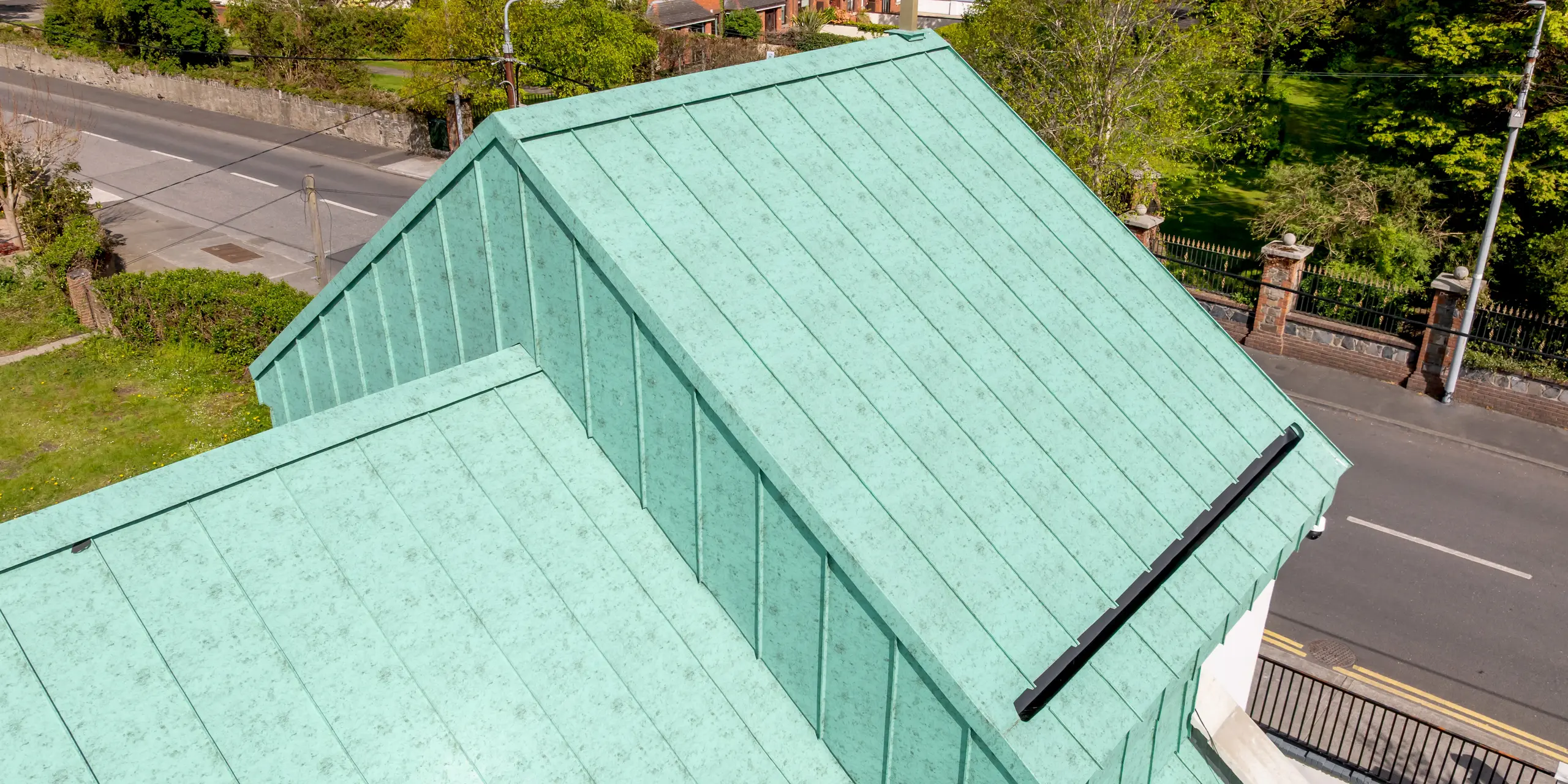 Detailreiche Drohnenaufnahme des PREFALZ Aluminium-Stehfalzdachs in P.10 Patinagrün auf der St. Thomas Orthodox Church in Dublin. Die großzügigen Dachflächen, die präzise ausgeführten Stehfalzlinien und der markante Giebel mit Kreuz bilden einen eindrucksvollen Blickfang. Die lebendige Patinaoptik erinnert an traditionelle Kupferdächer und verleiht dem Sakralbau eine zeitlose, hochwertige Ausstrahlung. Dank seiner hohen Formbarkeit fügt sich das PREFA Aluminium perfekt in die anspruchsvolle Dachgeometrie ein. Gleichzeitig überzeugt die langlebige Dachlösung durch Korrosionsbeständigkeit, geringes Gewicht, Wartungsarmut und nachhaltige Qualität für moderne Architektur.