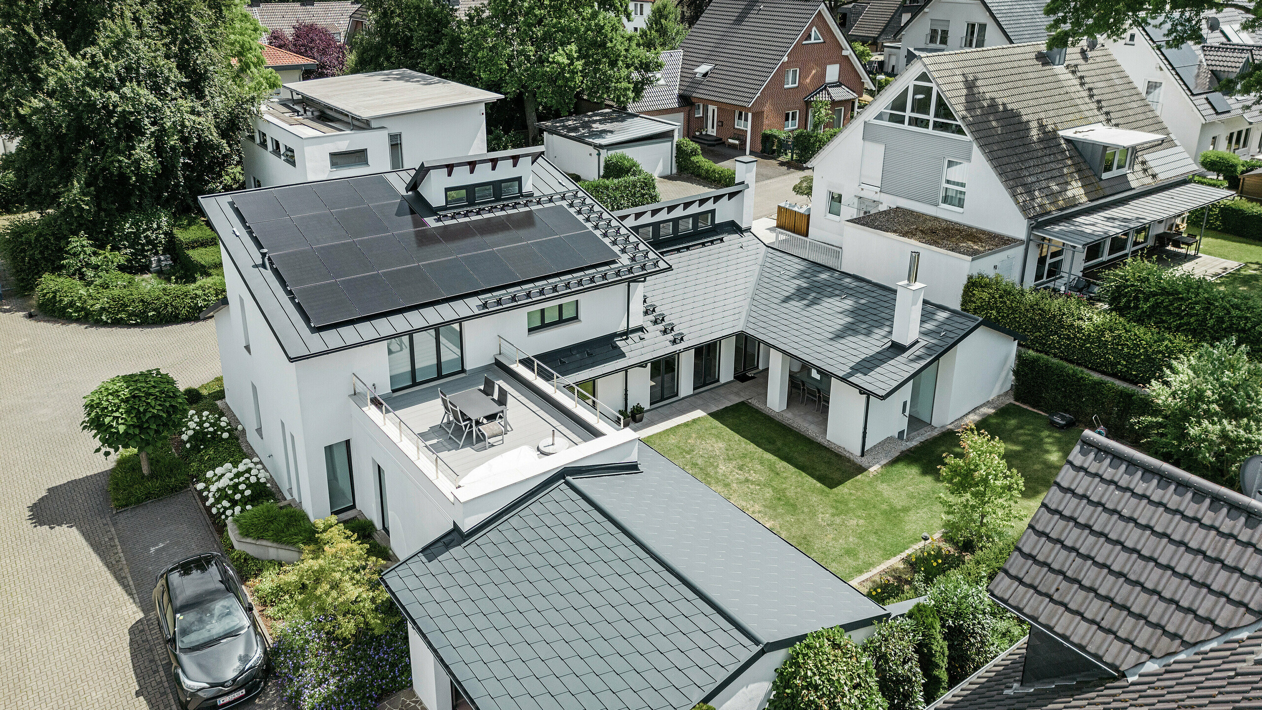 Pohľad z vtáčej perspektívy na výnimočnú strešnú krajinu rodinného domu v Dortmunde so strešnými šindľami PREFA DS.19 a PREFALZ v antracitovej farbe P.10, ako aj s veľkoplošným fotovoltaickým systémom