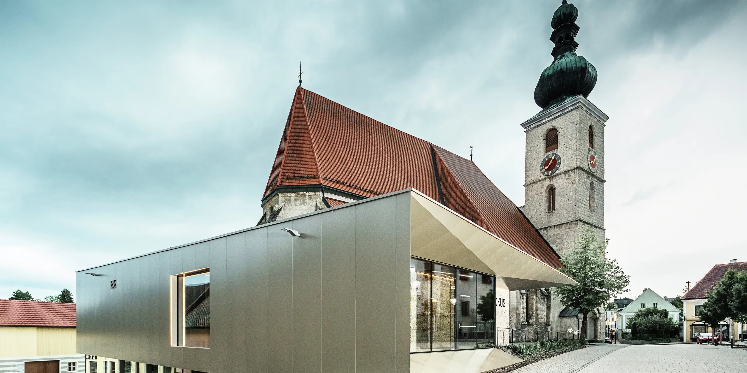 Bočný pohľad ukazuje filigránový previs strechy, realizovaný s použitím vysoko kvalitných hliníkových kompozitných panelov PREFA. Presné spracovanie umožňuje moderný vzhľad s čistými líniami a podčiarkuje architektonické prepojenie medzi starým a novým.