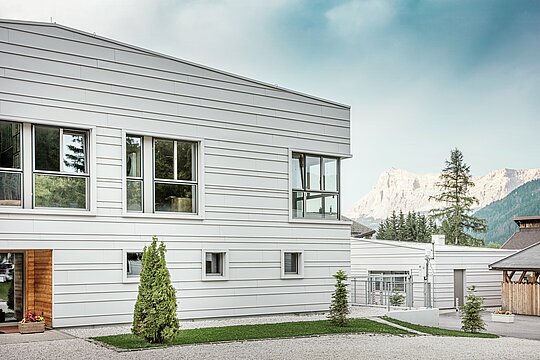 Detailný pohľad na kasárne „Tempesti“ s presne položenými pásmi PREFALZ v farbe P.10 prefa biela. Čisté línie horizontálne položeného stojatého falcového krytia zdôrazňujú moderný dizajn fasády. Svetlý povrch odráža slnečné svetlo a optimalizuje mikroklímu. V pozadí sa týčia impozantné hory Južného Tirolska – tu sa technika stretáva s prírodou na najvyššej úrovni.