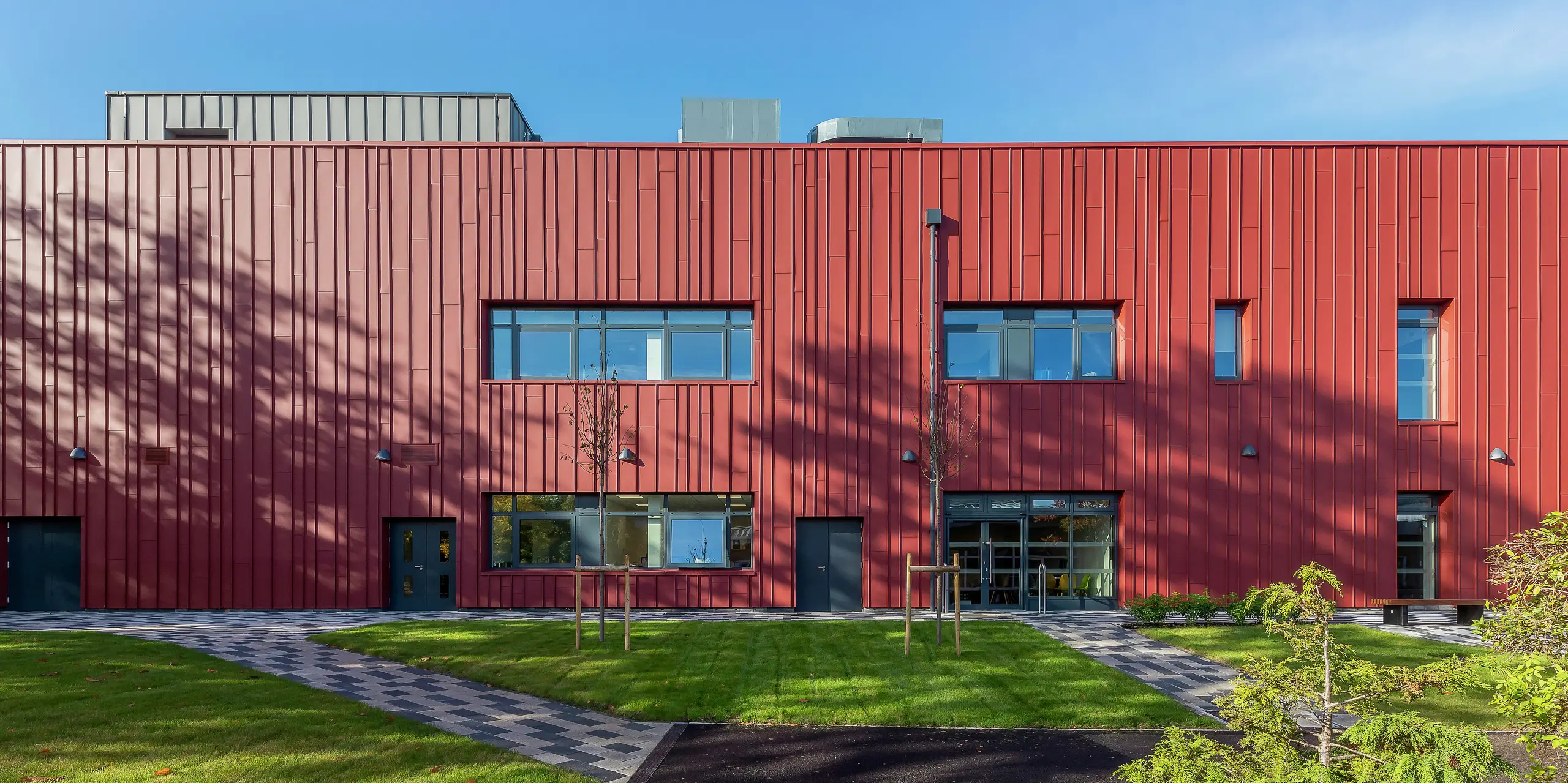 Moderný dizajn fasády s PREFALZ: Soldiers' Centre v Pirbright zaujme svojím vysokokvalitným obložením z PREFALZ v P.10 tmavočervená. Štýlová kombinácia s obložením okien v P.10 Anthrazit dodáva sociálnemu centru armády výrazný vzhľad. Tu sa spája funkčnosť a dizajn – udržateľný architektonický koncept s odolným hliníkom.