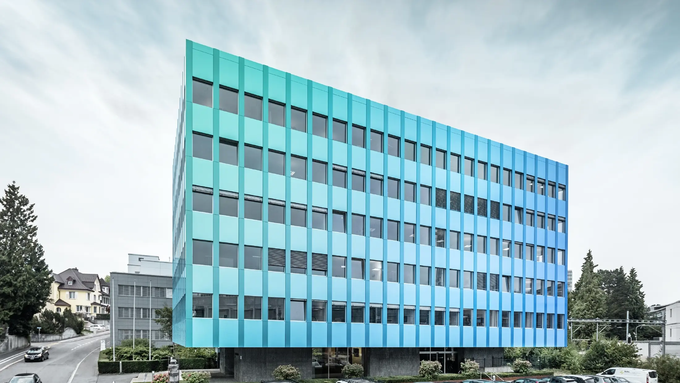 Bočný pohľad na Wielandhaus v Aarau; fasáda je obložená PREFABOND hliníkový kompozitný panel od spoločnosti PREFA, ktorý vďaka špeciálnemu procesu povrchovej úpravy žiaria modro-zelenou farbou.