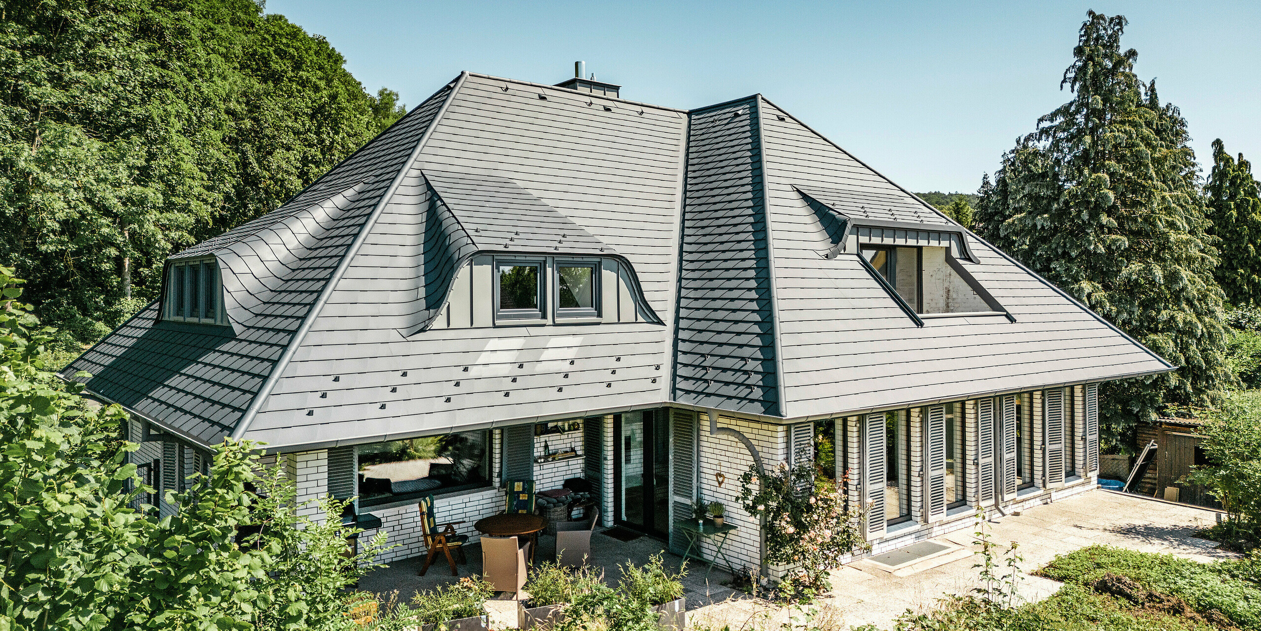 Samostatne stojaci dom s veľkolepou strechou pokrytou strešnými šindľami PREFA v antracitovej farbe P.10