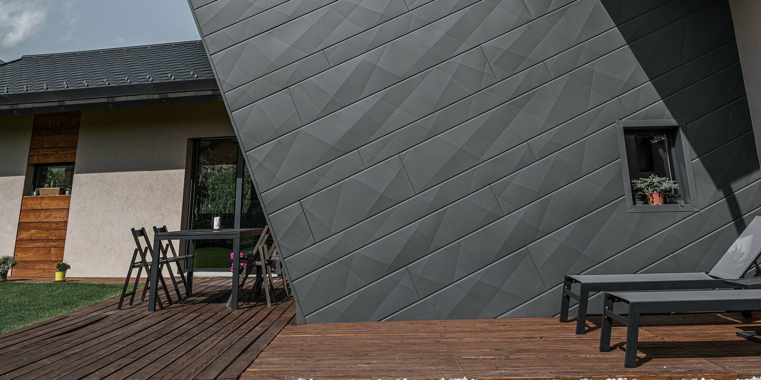 Pohľad na vilu Tia v Gressane, Taliansko, s kompletným systémom PREFA. Budova sa vyznačuje fasádou s diagonálne uloženými panelmi Siding.X v tmavošedej farbe P.10. Kombinácia tmavého hliníka a teplých drevených prvkov konštrukcie terasy znamená moderný dizajn a udržateľné stavebné materiály.