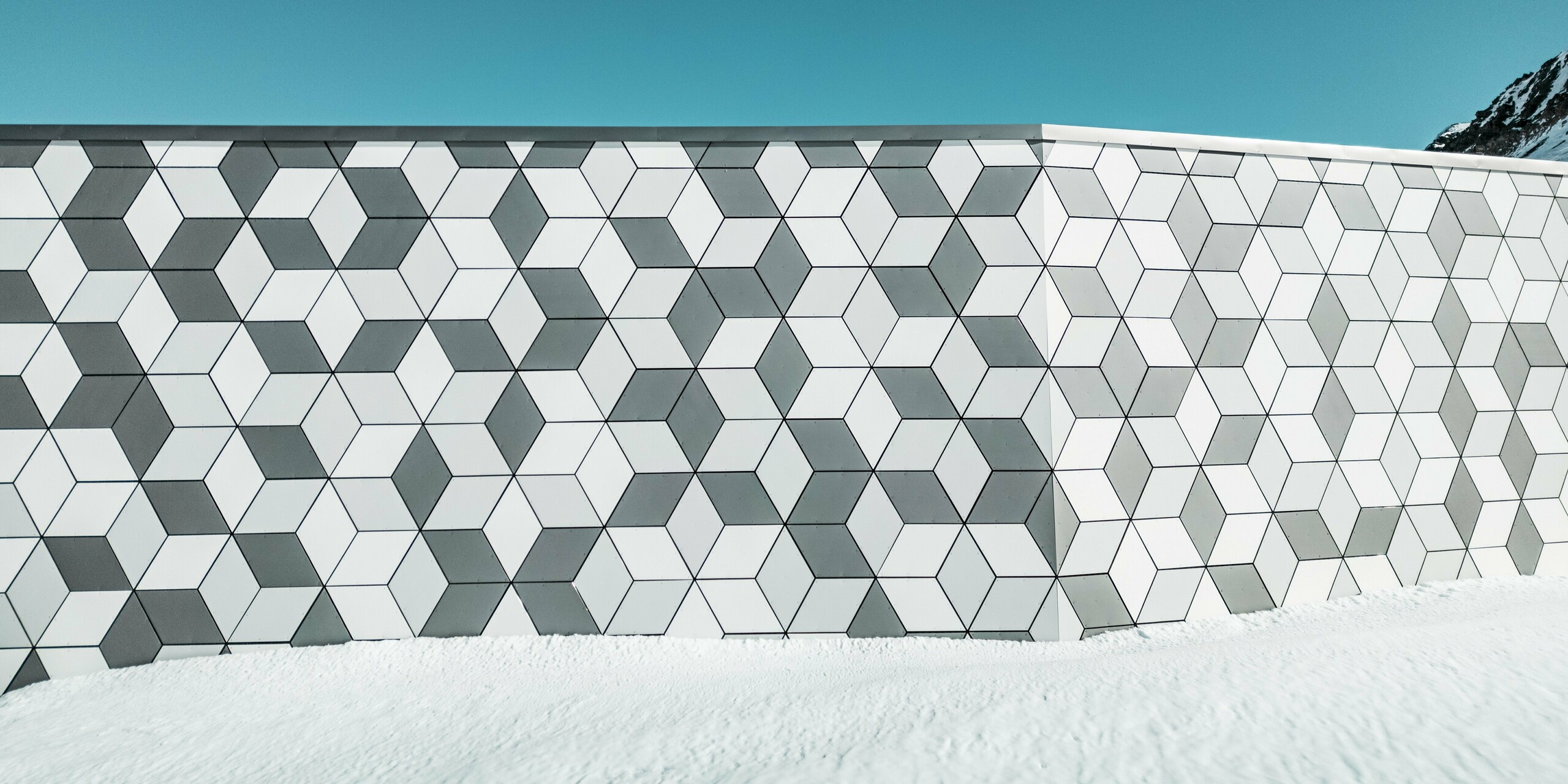 Detailný záber na fasádu stanice lanovky Jandri v Les Deux Alpes ukazuje presné usporiadanie diamantov z hliníkových kompozitných panelov PREFABOND. Diamanty sú usporiadané do pútavého vzoru. Vďaka harmonickej farebnej schéme v rôznych odtieňoch bielej a sivej farby fasáda dokonale ladí so zasneženou alpskou krajinou. Robustné panely odolné voči poveternostným vplyvom sú odolným a estetickým riešením pre extrémne poveternostné podmienky v horách.