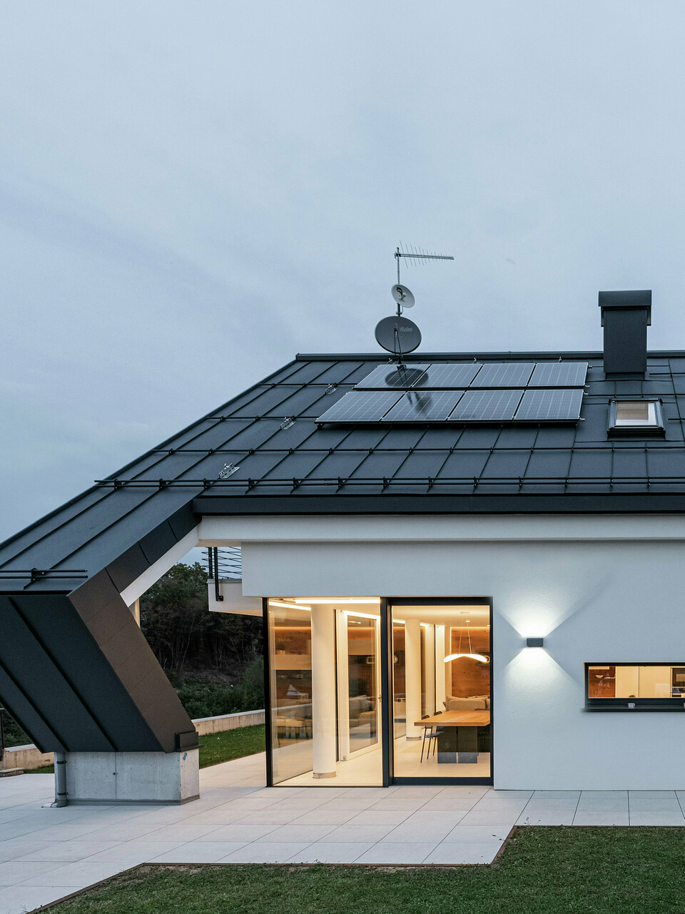 Moderný rodinný dom v Borgo Valbelluna v Taliansku s nápadnou šikmou strechou z materiálu PREFALZ vo farbe P.10 antracit. Odolná hliníková strešná krytina poskytuje optimálnu ochranu pred poveternostnými vplyvmi a zaujme flexibilnými možnosťami montáže. Integrované fotovoltické moduly efektívne využívajú povrch strechy na udržateľnú výrobu energie. Kombinácia hliníkovej strechy antracitovej farby a bielej fasády, ako aj nápadný presah šikmej strechy podčiarkujú elegantný a nadčasový dizajn budovy.