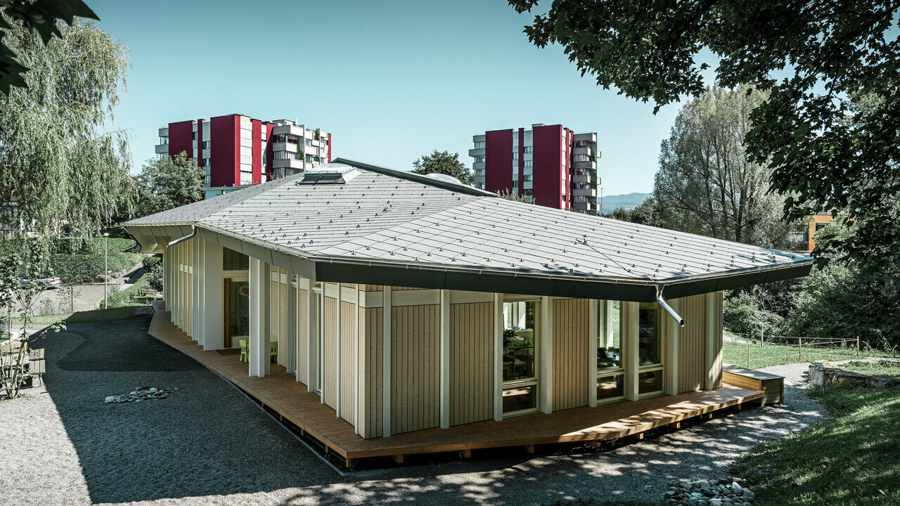 Jednoposchodová materská škola so zvislými fasádnymi panelmi a hliníkovou strechou PREFA (strešná šablóna) vo farbe svetlošedá