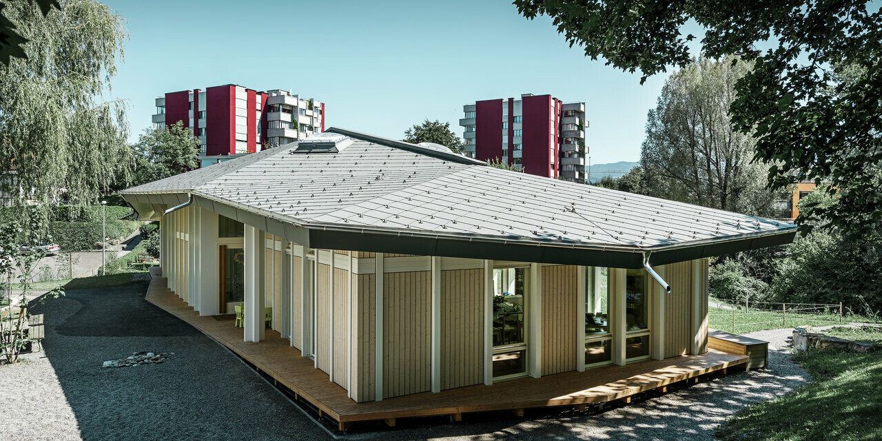 Jednoposchodová materská škola so zvislými fasádnymi panelmi a hliníkovou strechou PREFA (strešná šablóna) vo farbe svetlošedá