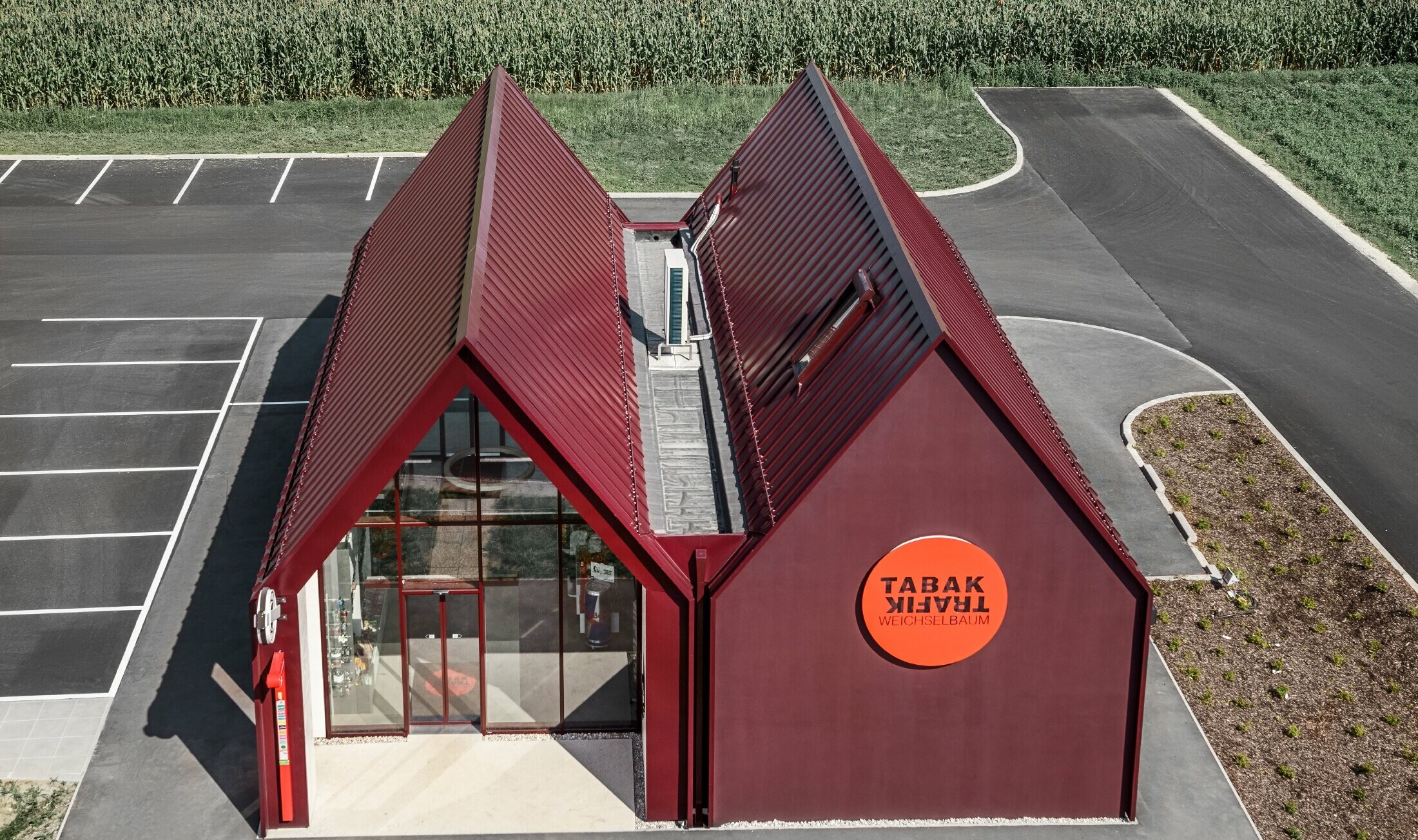 Moderná predajňa tabaku so sedlovou strechou s priamym prechodom na fasádu, s hliníkovým plášťom na dvojitú stojatú a uhlovú stojatú drážku v PREFA špeciálnej farbe čiernočervená