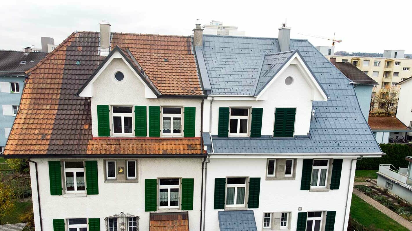 Polovica dvojdomu v Švajčiarsku; ľavá časť budovy ešte nebola zrekonštruovaná a sú na nej fľakaté pálené škridle. Pravá časť domu bola pokrytá PREFA falcovanými strešnými škridlami vo farbe kamenná šedá.