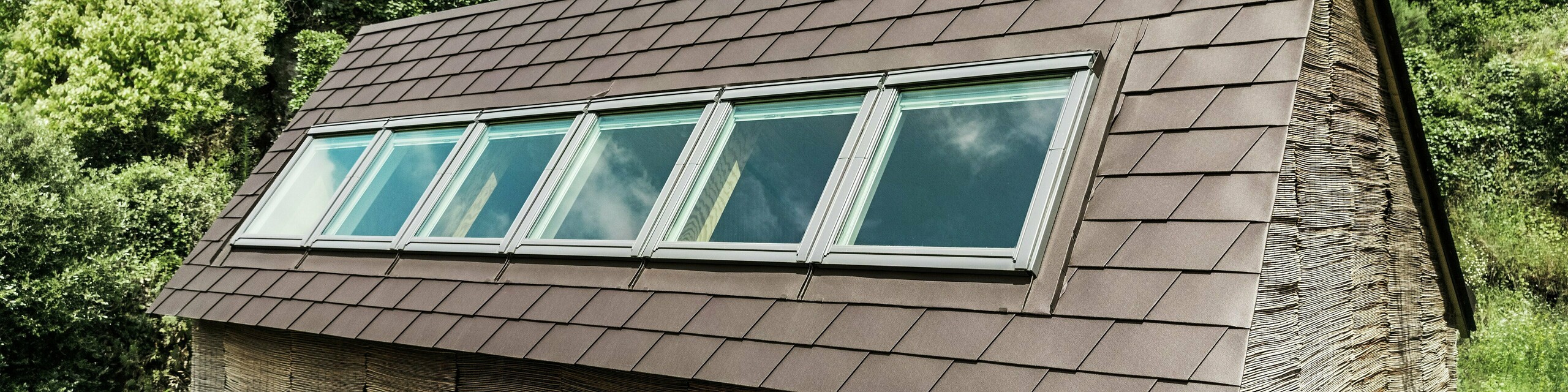 Strešné šindle PREFA v orieškovohnedej farbe P.10 na streche moderného domu so strešnými oknami - odolné hliníkové strešné riešenie pre energeticky úsporný a štýlový dizajn strechy