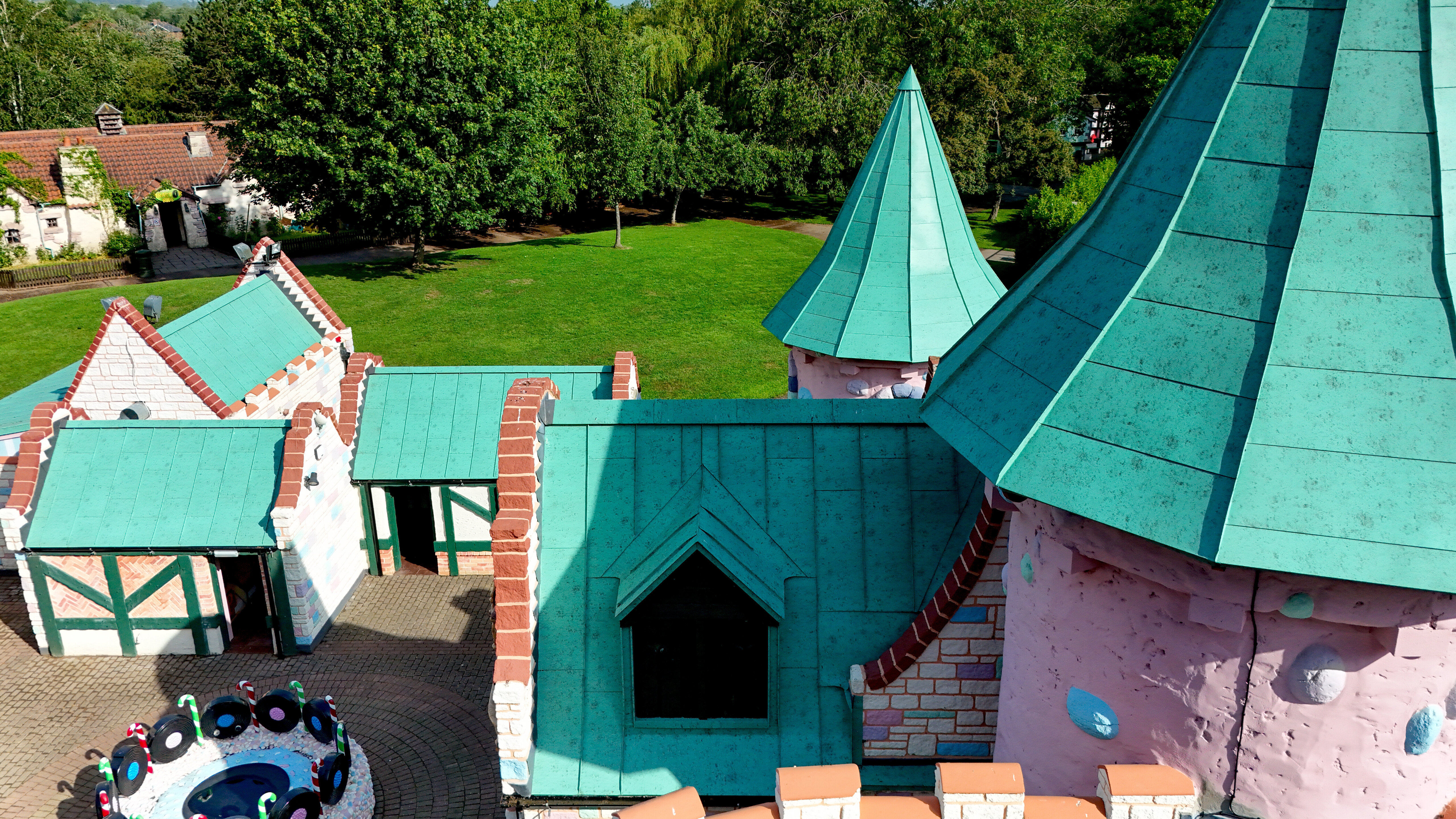 Detailreiche Perspektive auf die fantasievolle Schlossarchitektur im Sundown Adventureland mit verspielten Türmen, prägnanten Giebeln und komplexen Dachlandschaften als visuelle Highlights. Die PREFALZ Aluminiumdächer in P.10 Patinagrün stechen als markante Eyecatcher hervor und unterstreichen die einzigartigen Formen mit klaren Stehfalzen. Selbst anspruchsvolle Geometrien werden präzise umgesetzt. Gleichzeitig bieten die PREFA Dächer maximale Langlebigkeit, Korrosionsbeständigkeit und zuverlässigen Schutz – ideal für dauerhaft hochwertige und wetterbeständige Architektur.